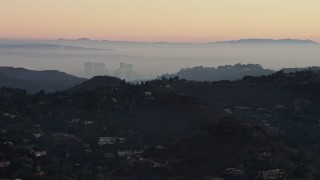 AX64_0156E - 5K aerial stock footage of Century City behind hilltop mansions in Hollywood Hills, California, twilight