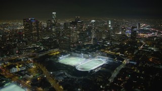 AX64_0354E - 5K aerial stock footage approach and fly over sports fields and Downtown Los Angeles skyline at night, California