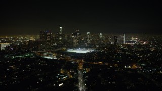AX64_0355 - 5K stock footage aerial video approach sports fields and Downtown Los Angeles skyline at night, California