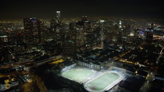 AX64_0356 - 5K stock footage aerial video fly over high school sports fields to approach Downtown Los Angeles skyscrapers, California, night