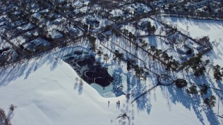 AX66_0022E - 4.8K aerial stock footage of a frozen pond and suburbs in snow, Old Westbury, New York
