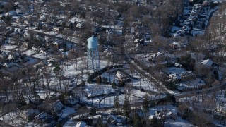 AX66_0029E - 4.8K aerial stock footage of a water tower in snow covered suburban neighborhood, Manhasset, New York