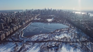 AX66_0102E - 4.8K aerial stock footage of over Central Park with snow and approach the icy reservoir, New York City