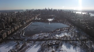 AX66_0103 - 4.8K aerial stock footage of over Central Park with snow and approach the icy reservoir, New York City