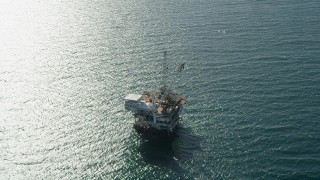 AX68_107 - 4.8K aerial stock footage of an oil drilling platform near sunlight reflected off the ocean near Long Beach, California