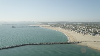 AX68_122 - 4.8K aerial stock footage fly over breakwater to approach the pier by beach and homes, Seal Beach, California