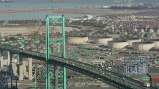 AX68_154 - 4.8K aerial stock footage of passing traffic on Vincent Thomas Bridge by cargo containers at the Port of Los Angeles, California