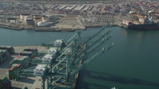 AX68_166 - 4.8K aerial stock footage fly over cargo cranes and pan to a ship docked at the Port of Los Angeles, California