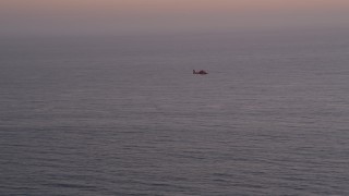 AX69_043 - 4.8K aerial stock footage of tracking a Coast Guard helicopter over the Pacific Ocean at twilight