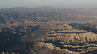 AX70_028 - 4K aerial stock footage Dry riverbed between mountain ridges near farms at sunrise, Cuyama, California