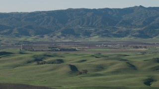 AX70_111 - 4K aerial stock footage Green hills and farms with mountains in the background in Hollister, California