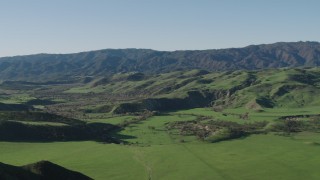 AX70_125 - 4K aerial stock footage Fly over a green hill to reveal a valley and mountains in Hollister, California