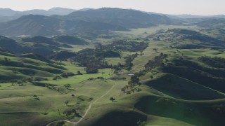AX70_163 - 4K aerial stock footage Flyby a country road leading to a small ranch, surrounded by green hills in Paicines, California