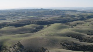 AX70_179 - 4K aerial stock footage Fly over dirt roads crossing hills to approach small farms in San Benito County, California