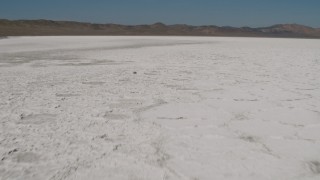 AX70_209 - 4K aerial stock footage Fly low over the surface of Soda Lake, California and tilt to reveal mountains