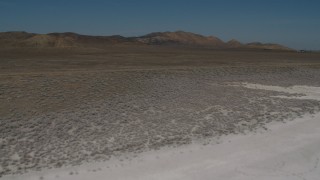 AX70_223 - 4K aerial stock footage Fly over Soda Lake and a desert road in California to approach desert mountains