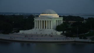 AX76_181E - 4.8K aerial stock footage approaching and flying by the Jefferson Memorial lit up for evening, Washington, D.C., twilight