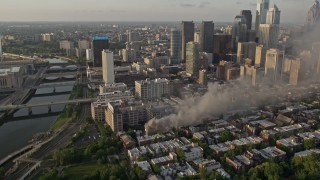 AX80_042 - 4.8K aerial stock footage of residential fire by the Downtown Philadelphia skyline, Pennsylvania, Sunset