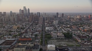 AX80_112E - 4.8K stock footage aerial video tilting from Broad Street and urban South Philly neighborhood to reveal and approach Downtown Philadelphia skyline, Pennsylvania, Sunset