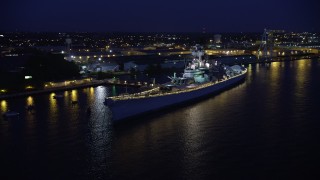 AX81_001 - 4.8K aerial stock footage approaching USS New Jersey battleship on the Delaware River, Camden, New Jersey, Night
