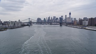 AX84_101E - 4K aerial stock footage tilt from ferry on the East River, and approach Manhattan and Brooklyn Bridge, Lower Manhattan skyline, New York City