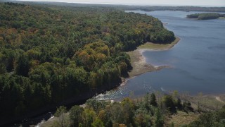 AX91_166 - 4K aerial stock footage of flying by lush forest on the shore in autumn, Lake Gallard, Connecticut
