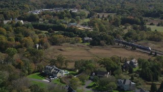 AX91_189 - 4K aerial stock footage of tracking a passenger train through forests and past businesses in autumn, Guilford, Connecticut