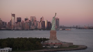 AX93_120 - 4K aerial stock footage Flying by Statue of Liberty, Lower Manhattan skyline, New York, sunset