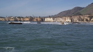 AXSF02_031 - 5K aerial stock footage of flying low over waves, reveal rock formations, homes on coastal cliffs, Shell Beach, California