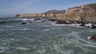 AXSF02_049 - 5K aerial stock footage of flying over waves rolling into rock formations, coastal cliffs, Avila Beach, California
