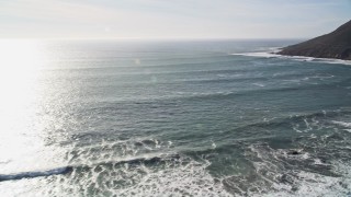 AXSF03_014 - 5K aerial stock footage video of flying over ocean waves, pan to reveal coastal hills, Cayucos, California