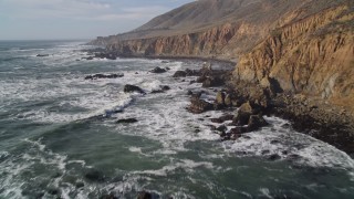 AXSF03_021 - 5K aerial stock footage of flying low over rugged coastal cliffs and ocean waves, Cambria, California