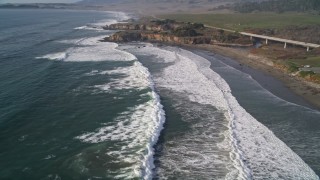 AXSF03_035 - 5K aerial stock footage pan from a small bridge and fly over ocean waves in San Simeon, California