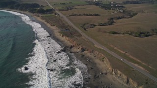 AXSF03_039 - 5K aerial stock footage flyby Highway 1 and pan left to ocean waves, a pier and an empty beach, San Simeon, California