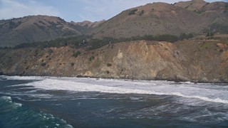 AXSF03_061 - 5K aerial stock footage of flying by waves rolling into coastal cliffs, San Simeon, California
