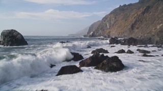 AXSF03_063 - 5K aerial stock footage flying low over waves crashing over rocks, coastal cliffs, San Simeon, California