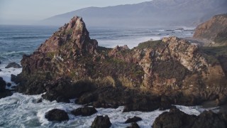 AXSF03_083 - 5K aerial stock footage approach and fly over giant rock formation, tilt to ocean waves, Big Sur, California