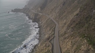 AXSF03_090 - 5K aerial stock footage of following Highway 1 coastal road on cliffs, tilt to a bird's eye view of a car on the road, Big Sur, California