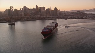 AXSF10_065 - 5K aerial stock footage of a cargo ship sailing under Bay Bridge, reveal Downtown San Francisco skyline, California, sunset