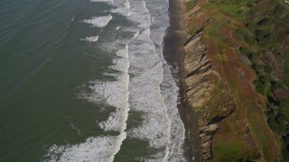 AXSF15_034 - 5K aerial stock footage of a reverse view of ocean waves rolling toward a beach and coastal cliffs, Lakeshore District, San Francisco, California
