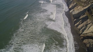 AXSF15_036 - 5K aerial stock footage of a reverse view of ocean waves rolling into coastal cliffs, Daly City, California