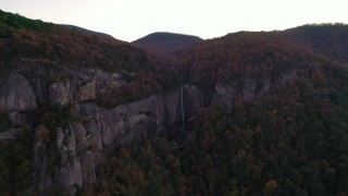 CAP_014_021 - 2.7K stock footage aerial video wide reverse view of forest and a clifftop waterfall at sunset, Chimney Rock, North Carolina