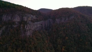 CAP_014_022 - 2.7K stock footage aerial video wide reverse view of forest, mountains, and a clifftop waterfall at sunset, Chimney Rock, North Carolina