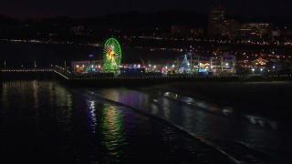 CAP_018_119 - HD stock footage aerial video approach the Ferris wheel and rides at nighttime from the ocean, Santa Monica Pier, California