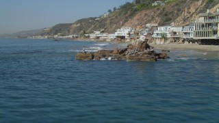 DCA05_106 - 4K aerial stock footage of flying by birds on a rock formation, coastal homes, Malibu, California