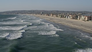 DCA08_231E - 4K aerial stock footage of flying low over waves rolling toward beach and homes, Mission Beach, California