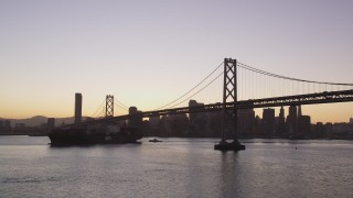 DCSF07_069 - Aerial stock footage of 5K Aerial Video Flying away from cargo ship sailing under the Bay Bridge, San Francisco, California, twilight