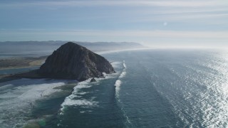 DFKSF03_013 - 5K aerial stock footage of flying over waves crashing into Morro Rock, coast, Morro Bay, California