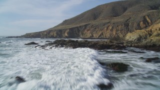 DFKSF03_026 - 5K aerial stock footage of flying low over waves crashing into coastal cliffs, Harmony, California