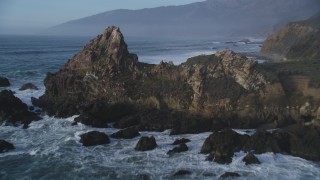 DFKSF03_104 - 5K stock footage aerial video approach and fly over giant rock formation, tilt to ocean waves, Big Sur, California